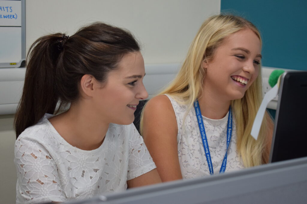 Two female staff members smiling and looking at a computer.