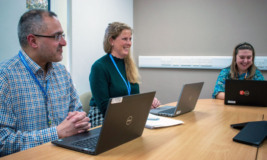 three members of staff chatting at their desk with their laptops