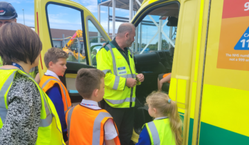 Group of primary school children wearing high-vis jackets stood near front door of ambulance