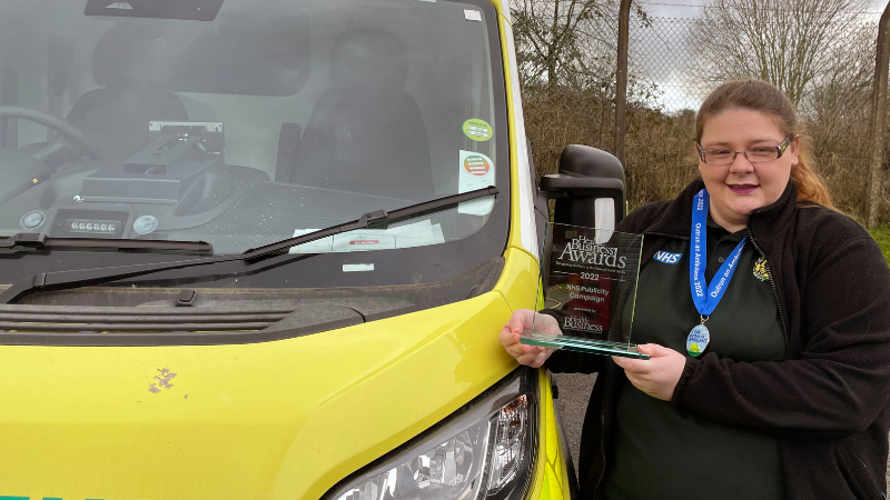 Emma, a lady with brown hair in a ponytail, stood next to an ambulance holding a glass trophy