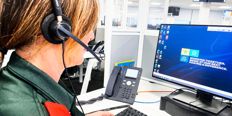 Female clinician with brown hair in ponytail wearing headset looking at computer screen