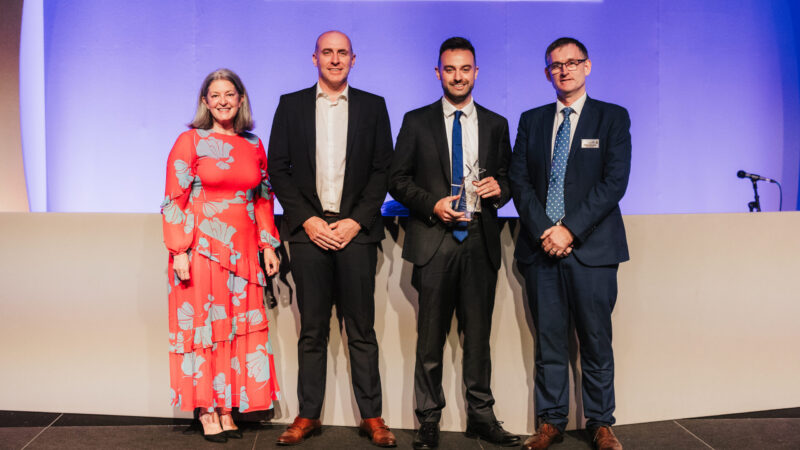 Four people stood on stage with Jack in the middle holding a trophy