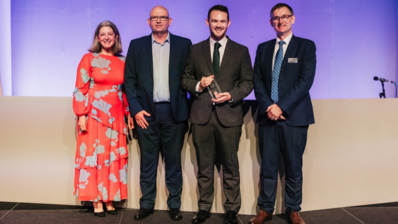 four people stood on stage with Martyn in the middle holding an award