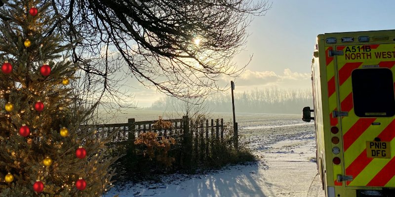 A frosty scenic view with an ambulance to the left and a Christmas tree to the right. The floor is covered in a light dusting of snow.